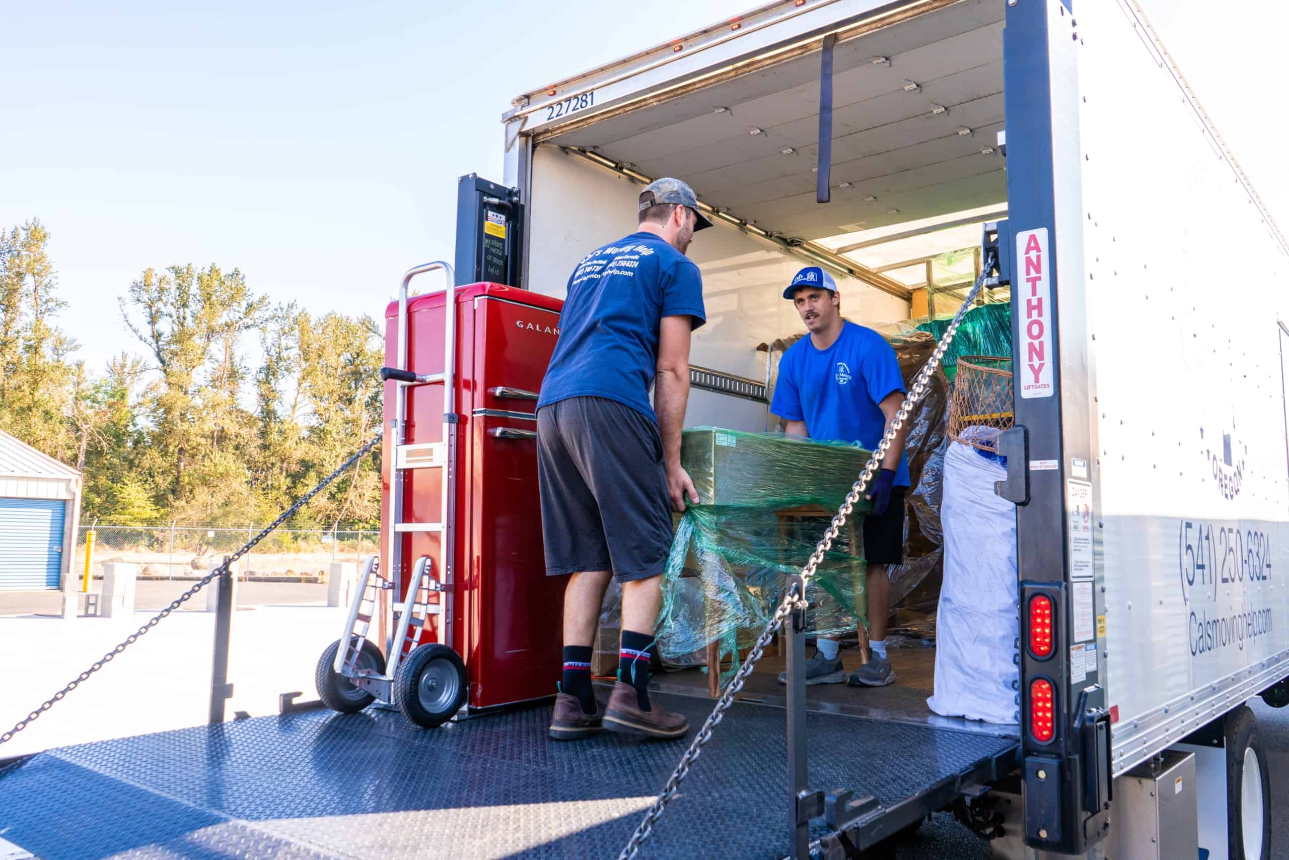 piece of furniture is being loaded onto a moving truck by two movers wearing blue branded apparel of cal's Moving & Storage