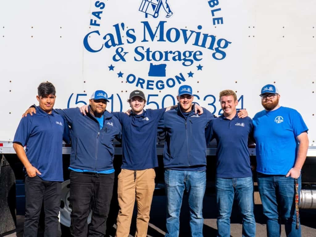 6 Cal's Moving & Storage team members stading in front of a branded moving track wearing blue branded tshirts and caps